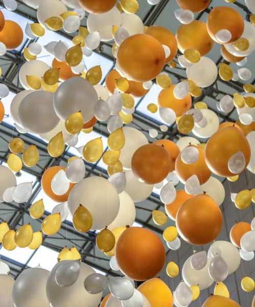 Vibrant arrangement of orange, white, and yellow balloons hanging in an indoor celebration space.